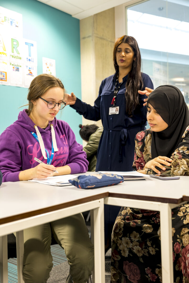 two esol students sat at a desk while a member of staff speaks to them