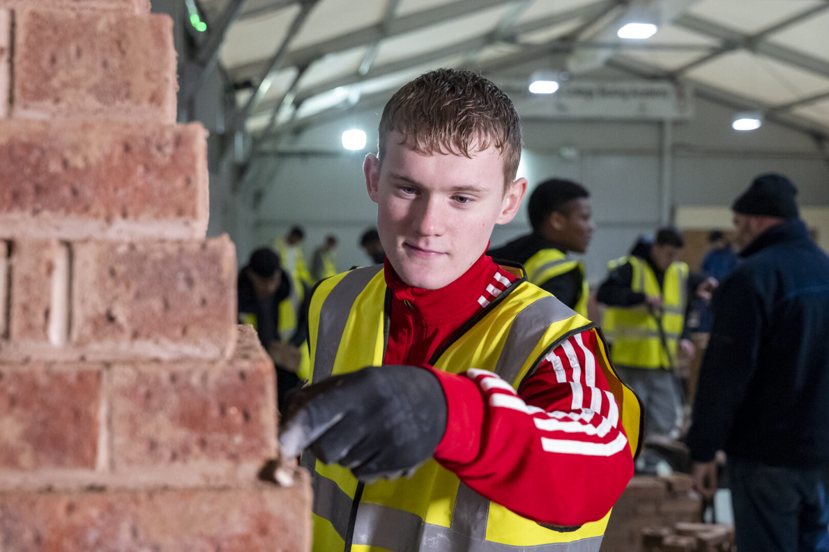 a brickwork student wearing a high visibility jacket cementing a wall of bricks