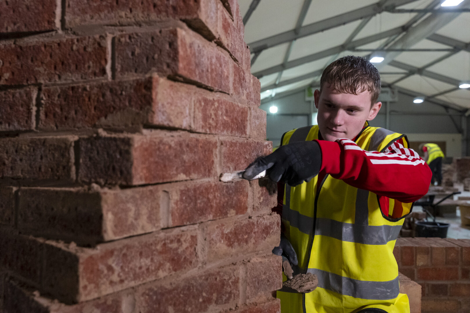 a brickwork student wearing a high visibility jacket cementing a wall of bricks
