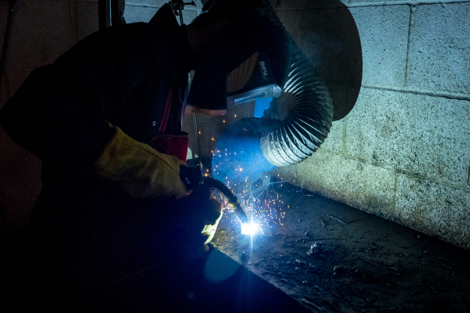 a welding student wearing a mask and working at a workbench as sparks fly from the welding equipment
