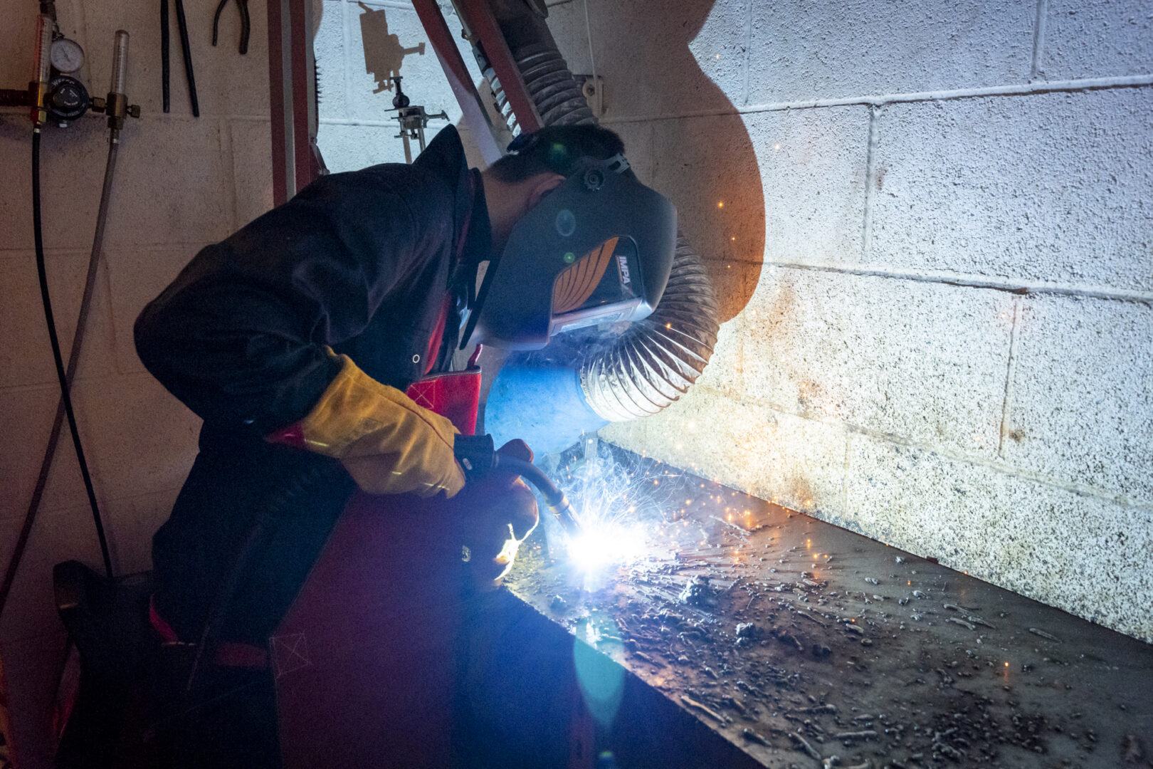 a welding student wearing a mask and working at a workbench as sparks fly from the welding equipment