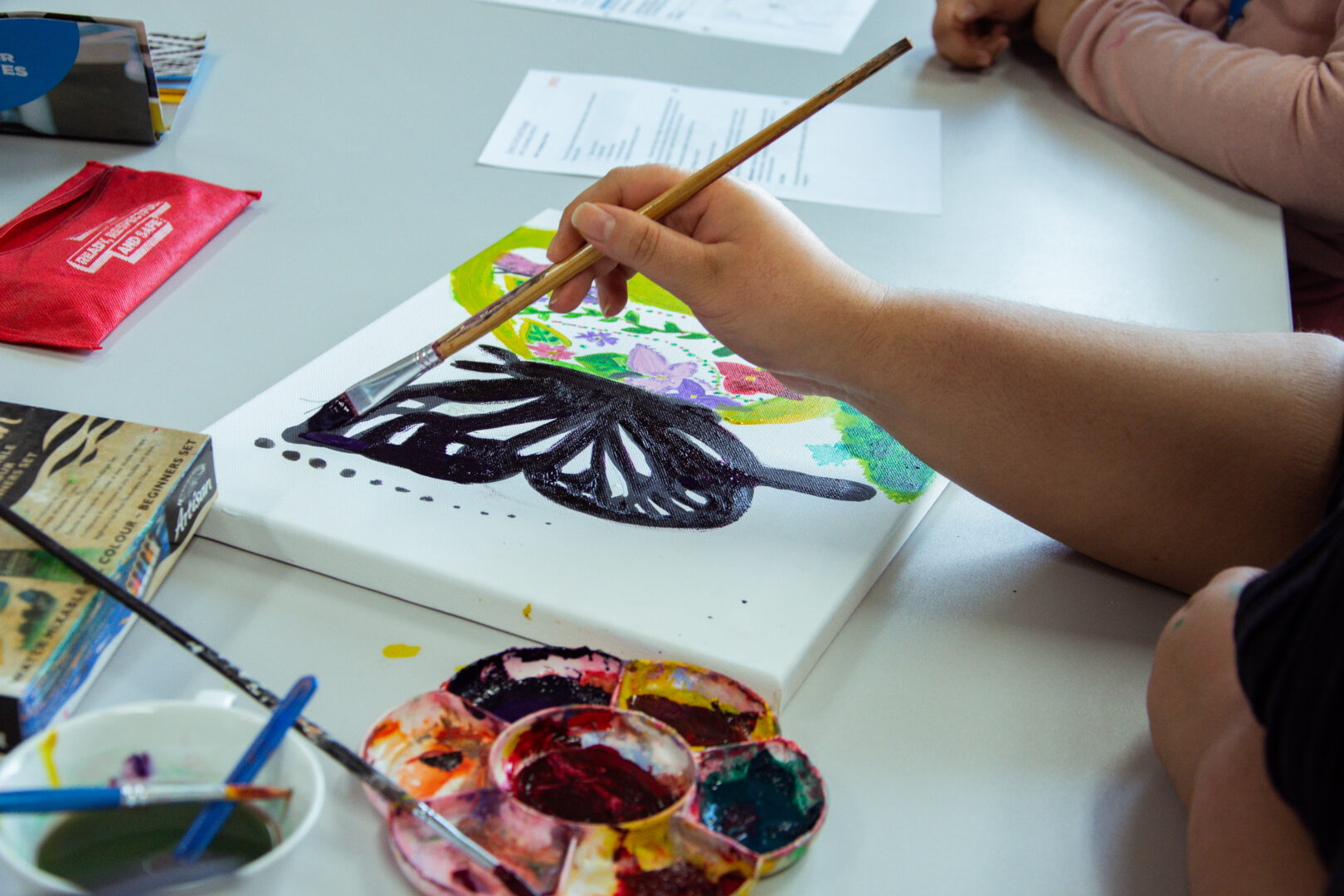 image of students hands painting a butterfly on a canvas