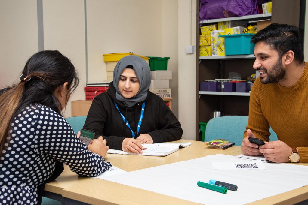 3 students sat at a desk discussing the work