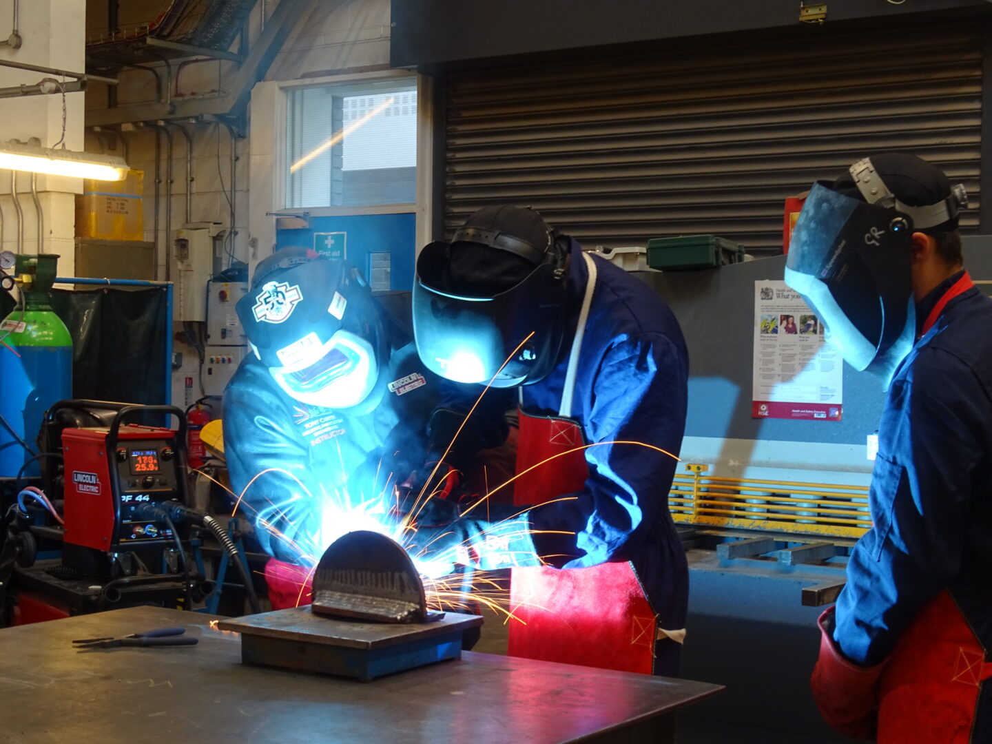 3 welding students working in a welding workshop as sparks fly