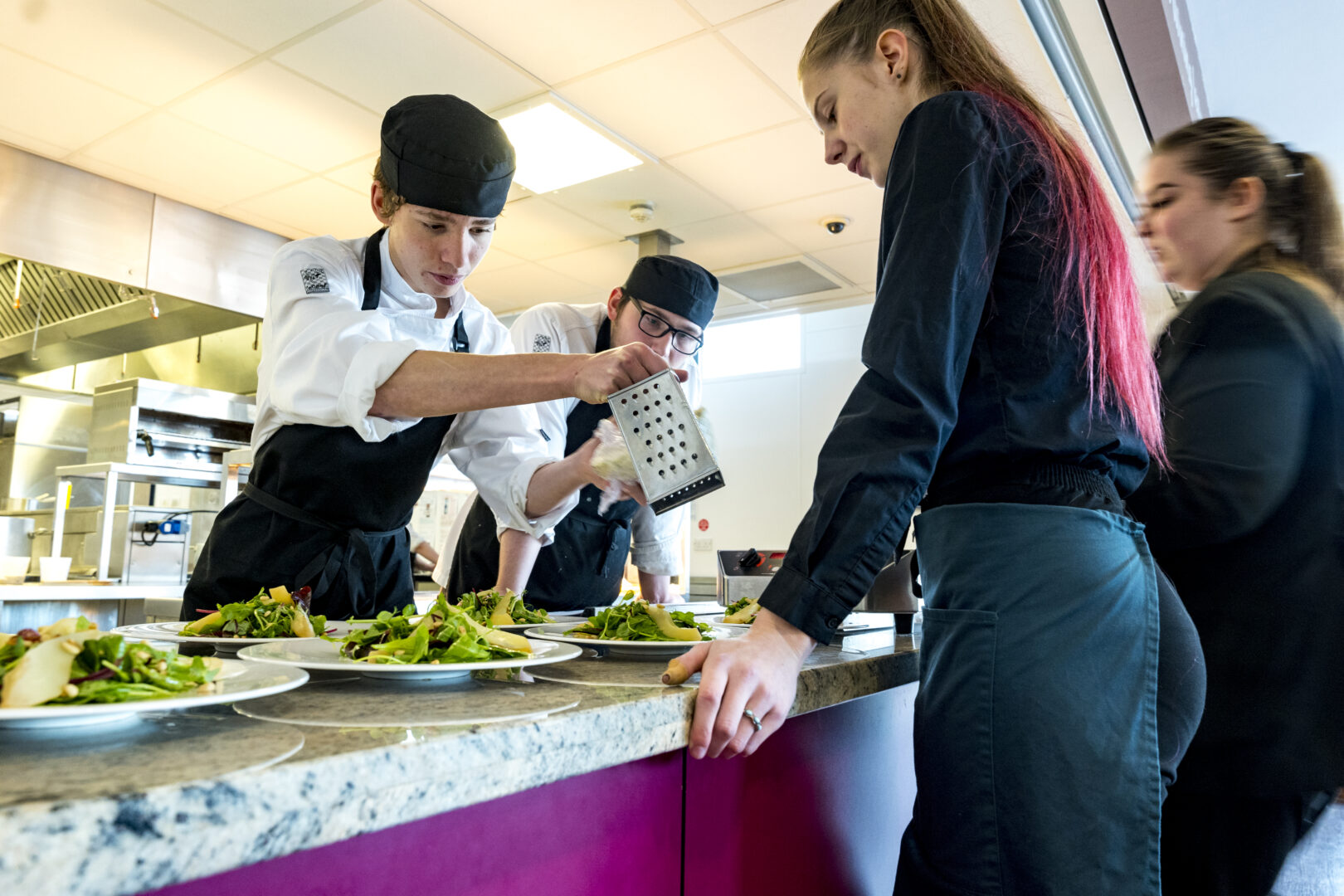 catering and hospitality students serving a salad to two students