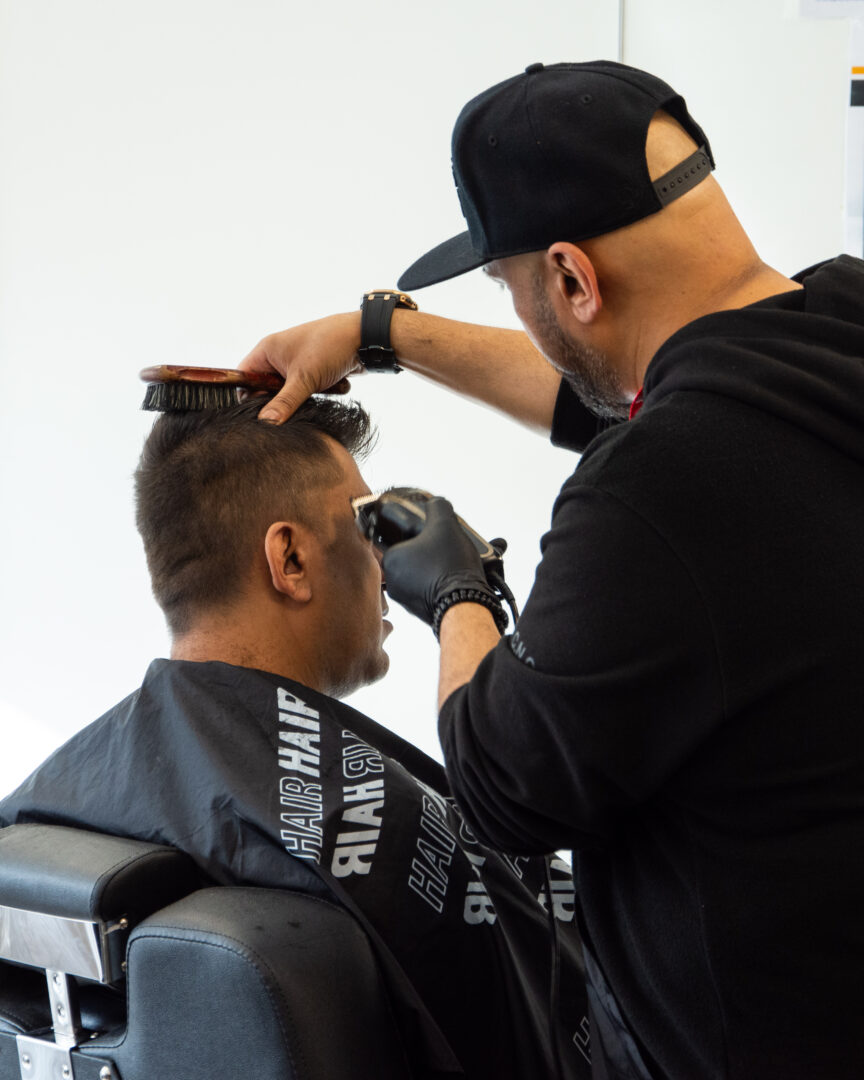 barbering student using a clipper to cut the hair of a model