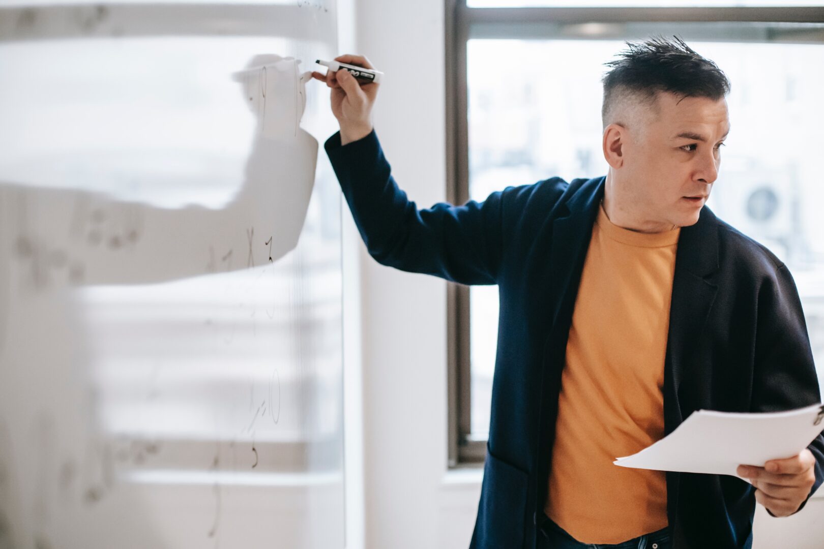 a teacher stood at a whiteboard writing as he teaches a secondary school class