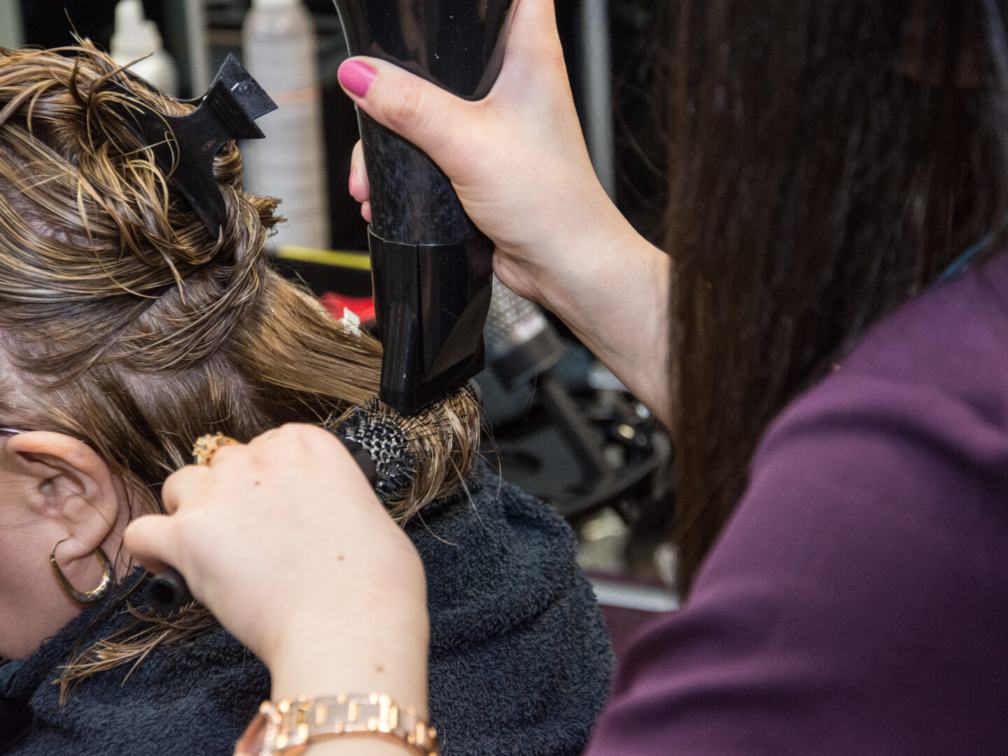 hair and beauty student using a rollerbrush to dry the hair of a hair model