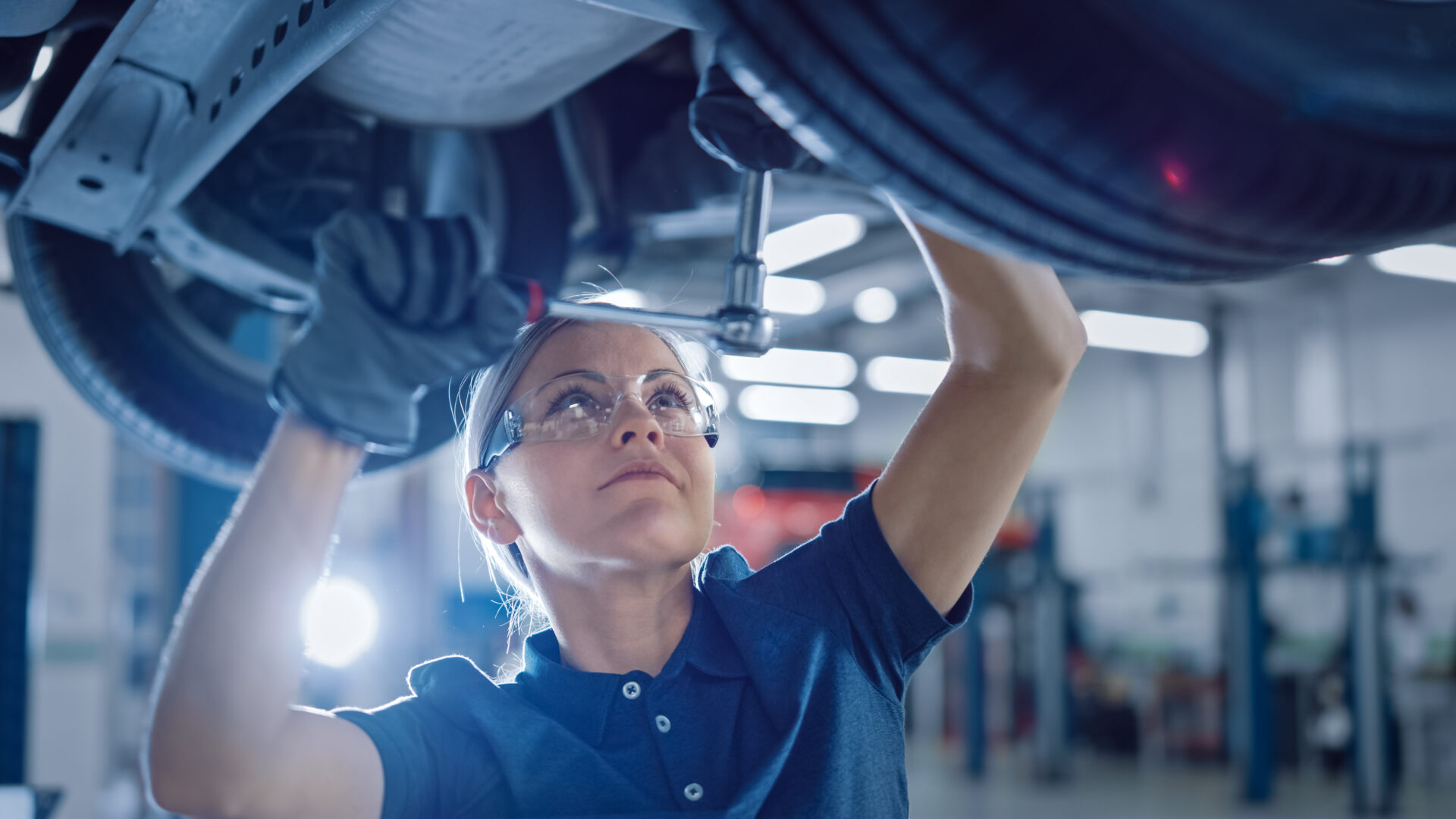 a female motor vehicle student wearing safety glasses using equipment to work on the underside of a vehicle