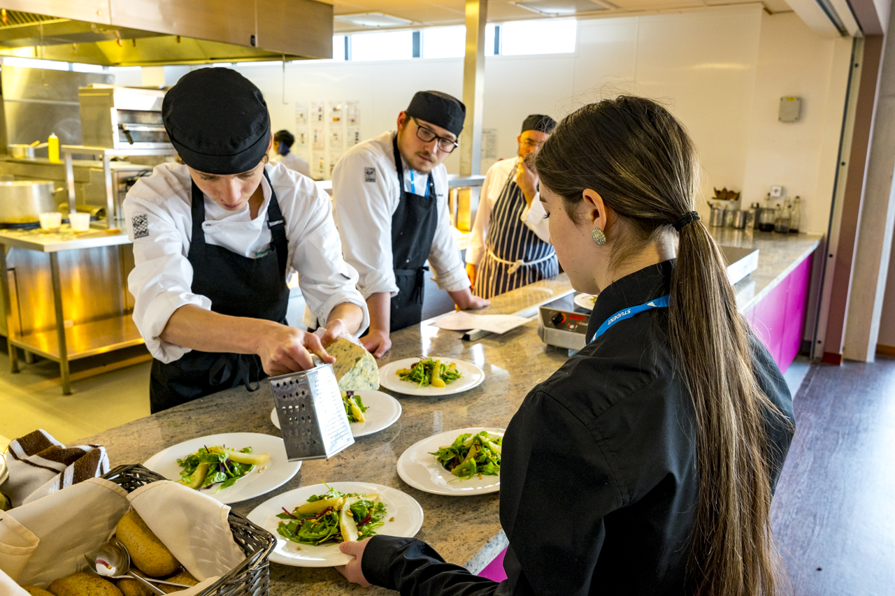 1 student in the foreground waiting to collect dishes from student chefs in the grove restaurant and bar