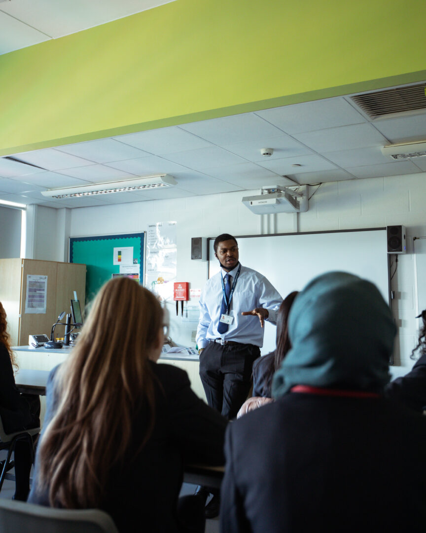 a teacher stood at the front of a classroom delivering a lesson