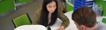 a student sat at a desk speaking with a member of staff regarding guidance