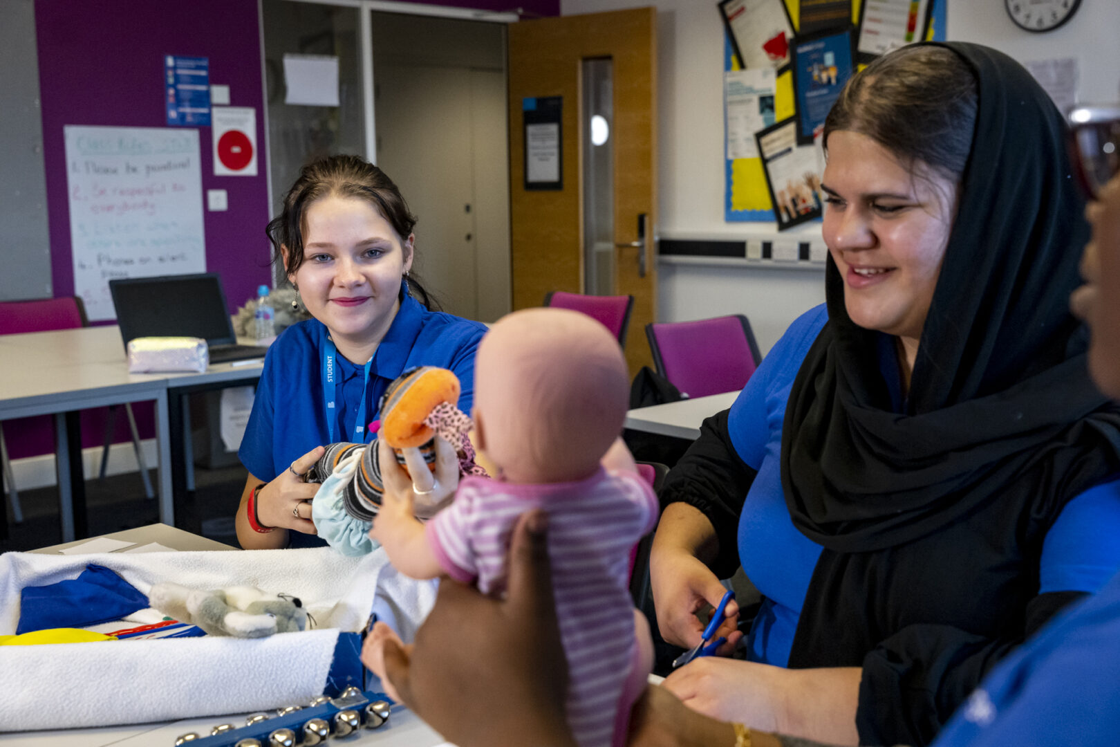 two smiling childcare students sat holding a baby doll