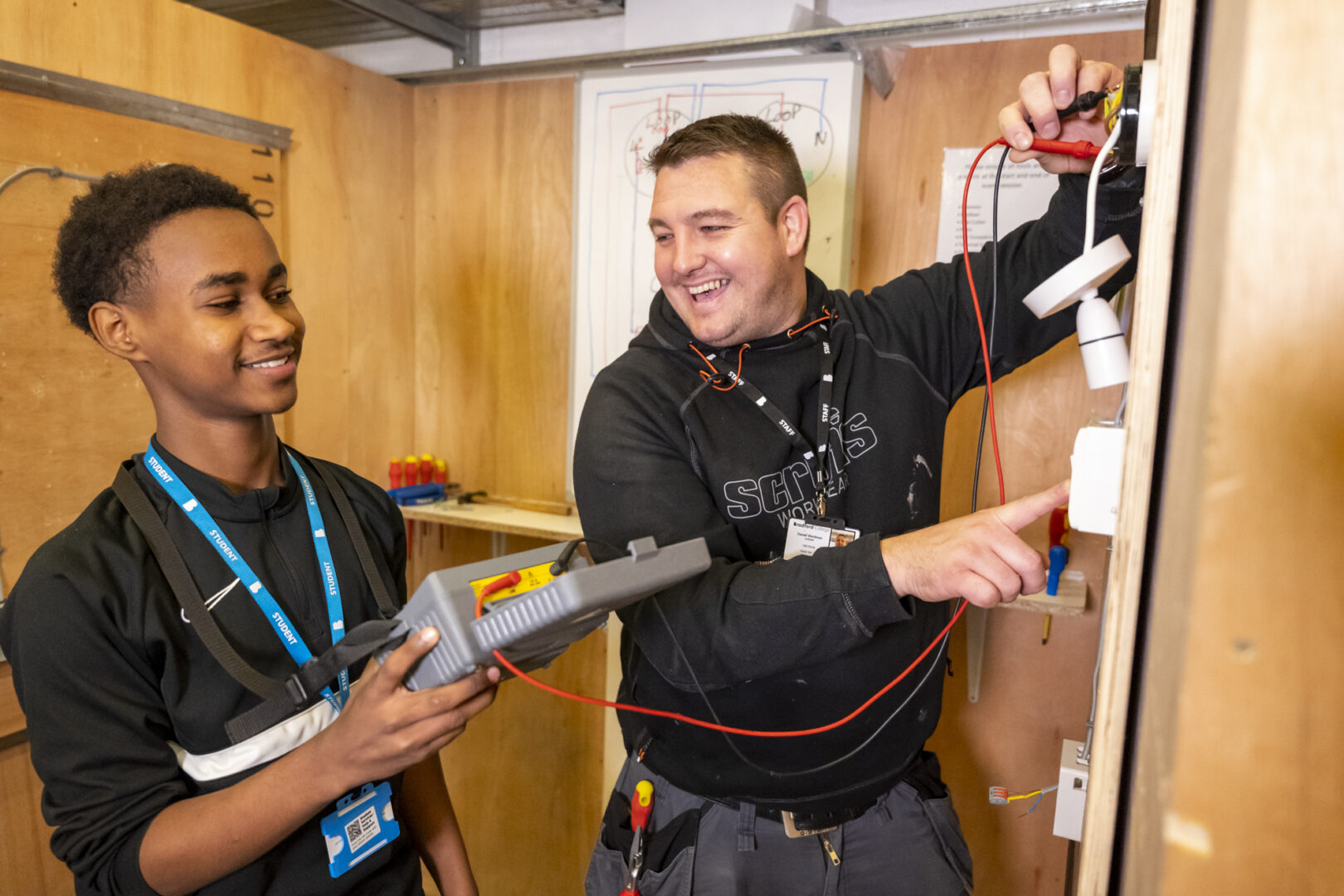 an electrical student practising techniques in the electric workshop with a tutor