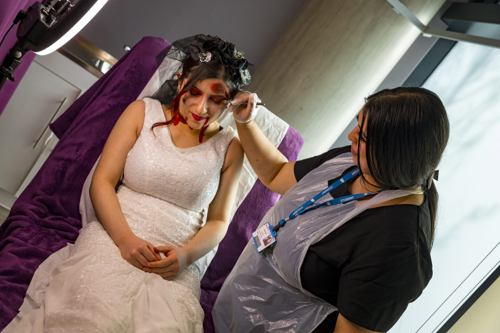 a media makeup student applying make up and prosthetics to a model dressed in a white dress
