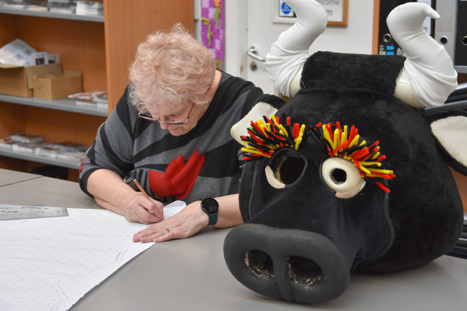 bradford school of art's sylvia Devanney drawing on fabric with the head of the bullgirl mascot on the table next to her