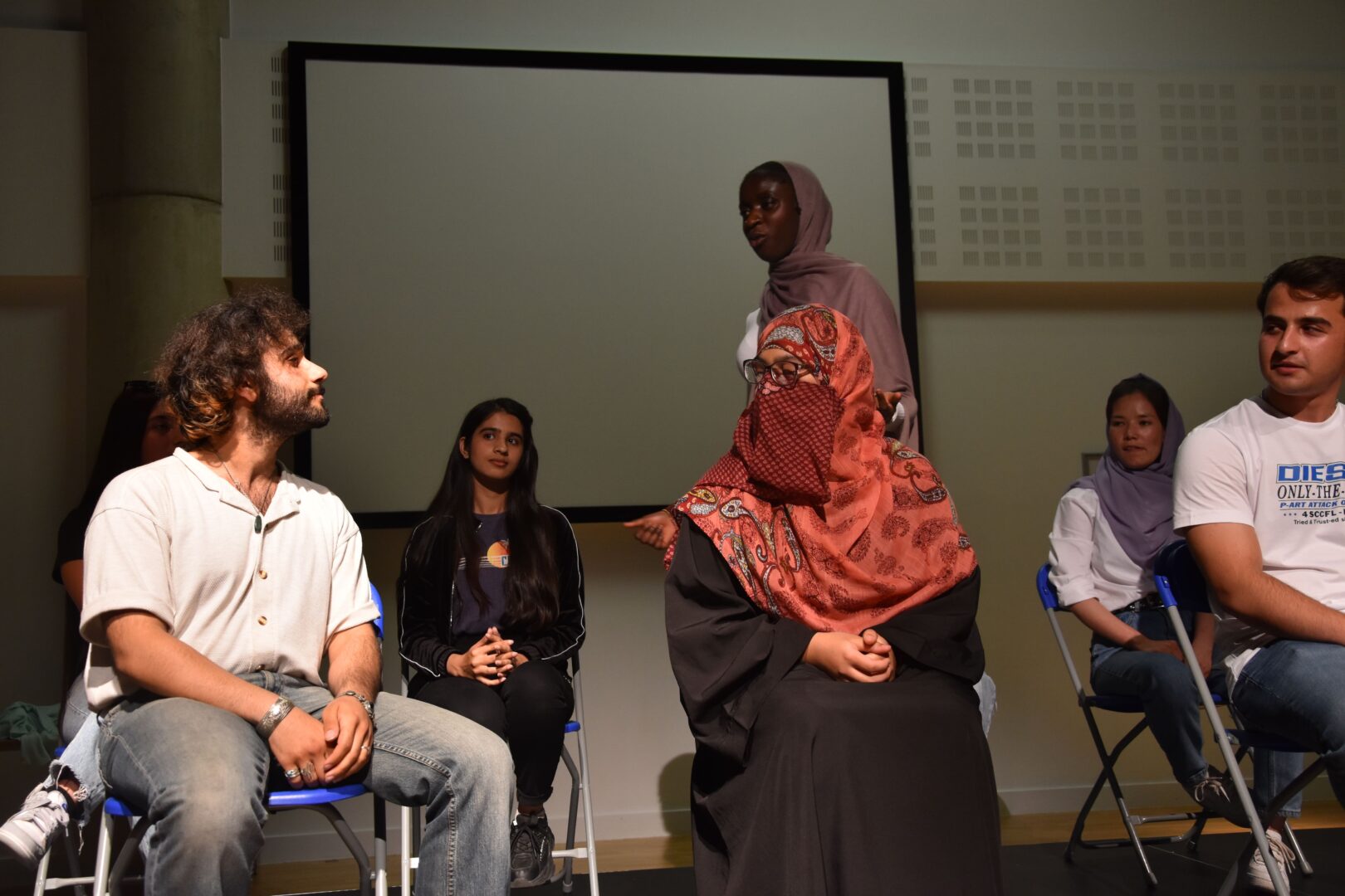 a group of esol students sat on stage as one student is stood performing