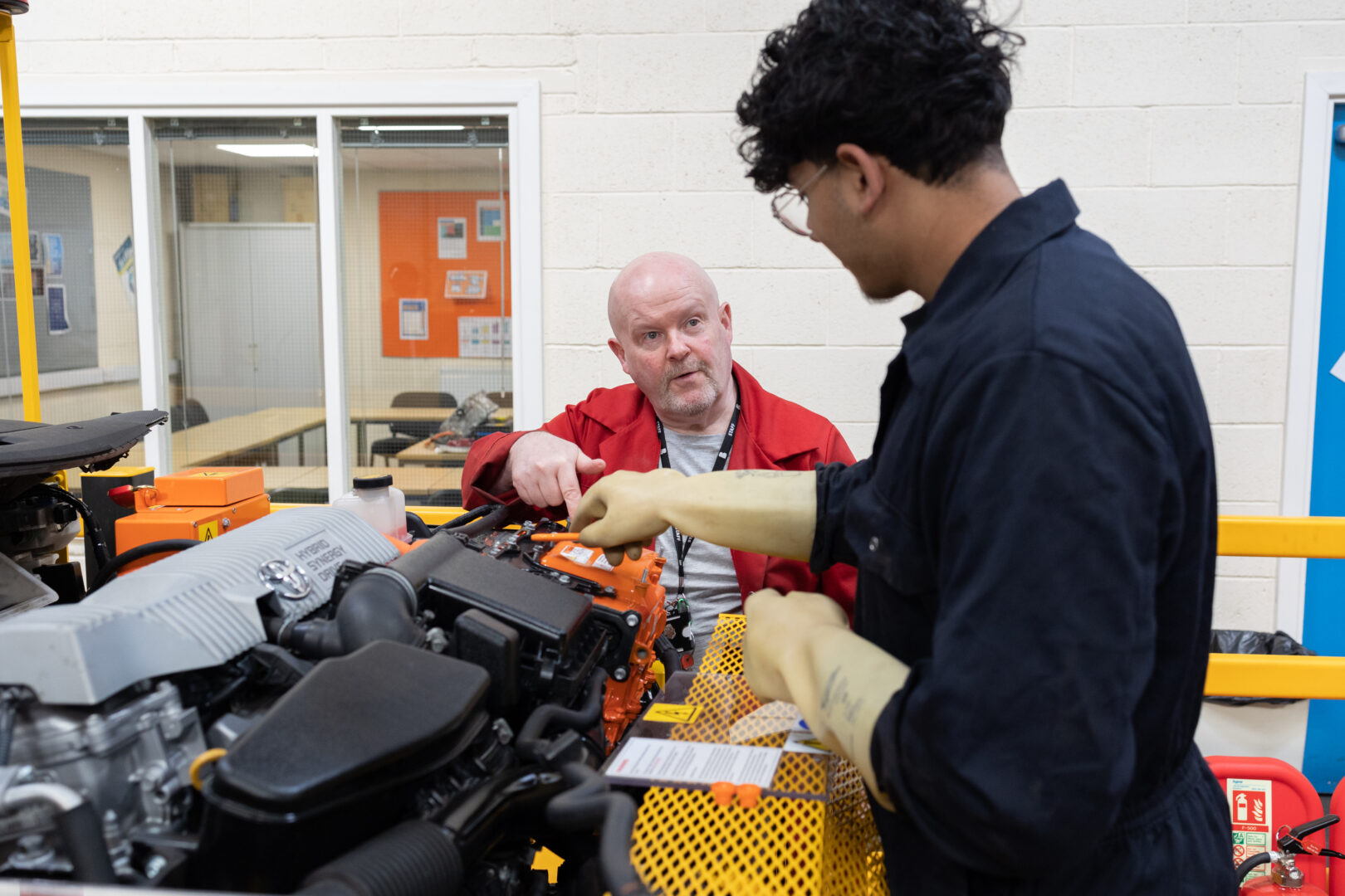 a motor vehicle student speaks to a tutor as he works on an electric engine