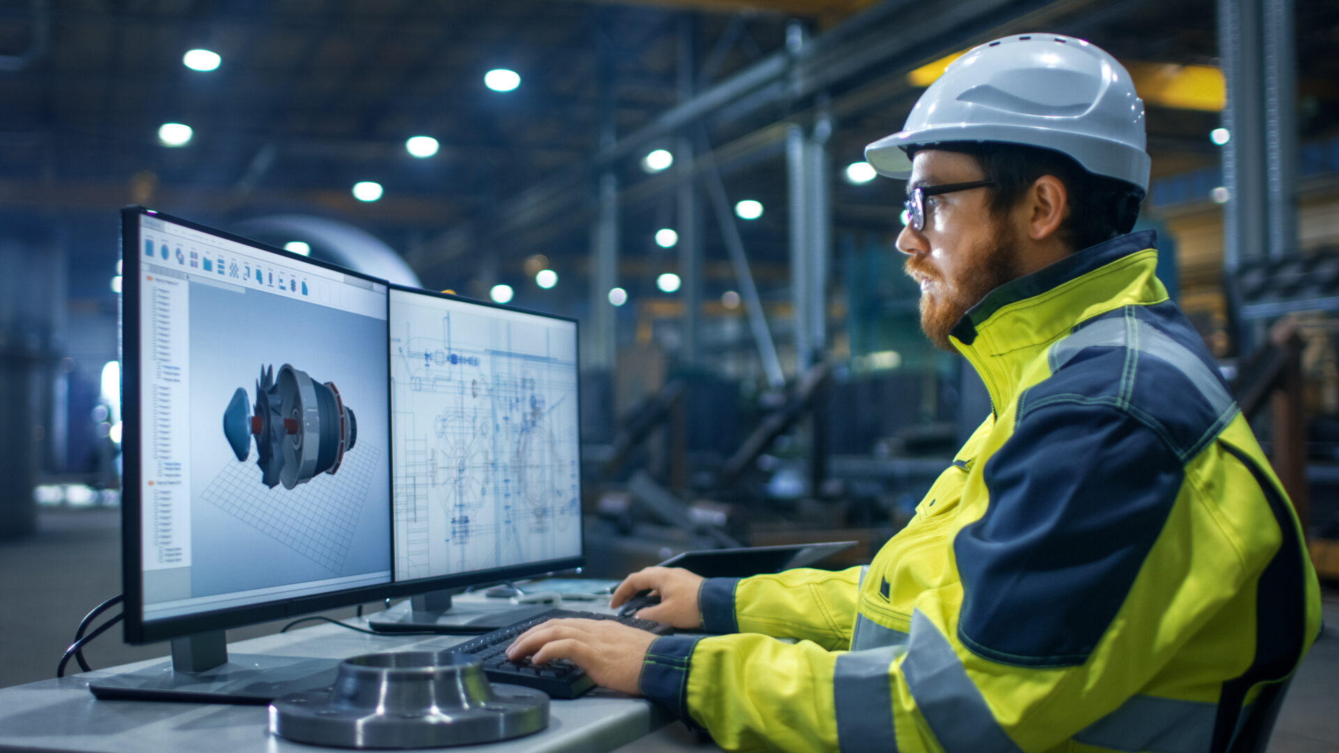 a student sat at a desk wearing a hard hat and high vis as they work on a computer screen