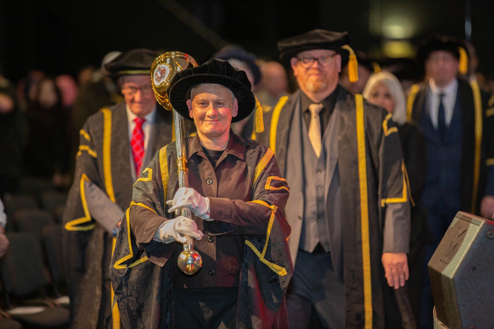 a member of staff holding a mace as they walk in a procession