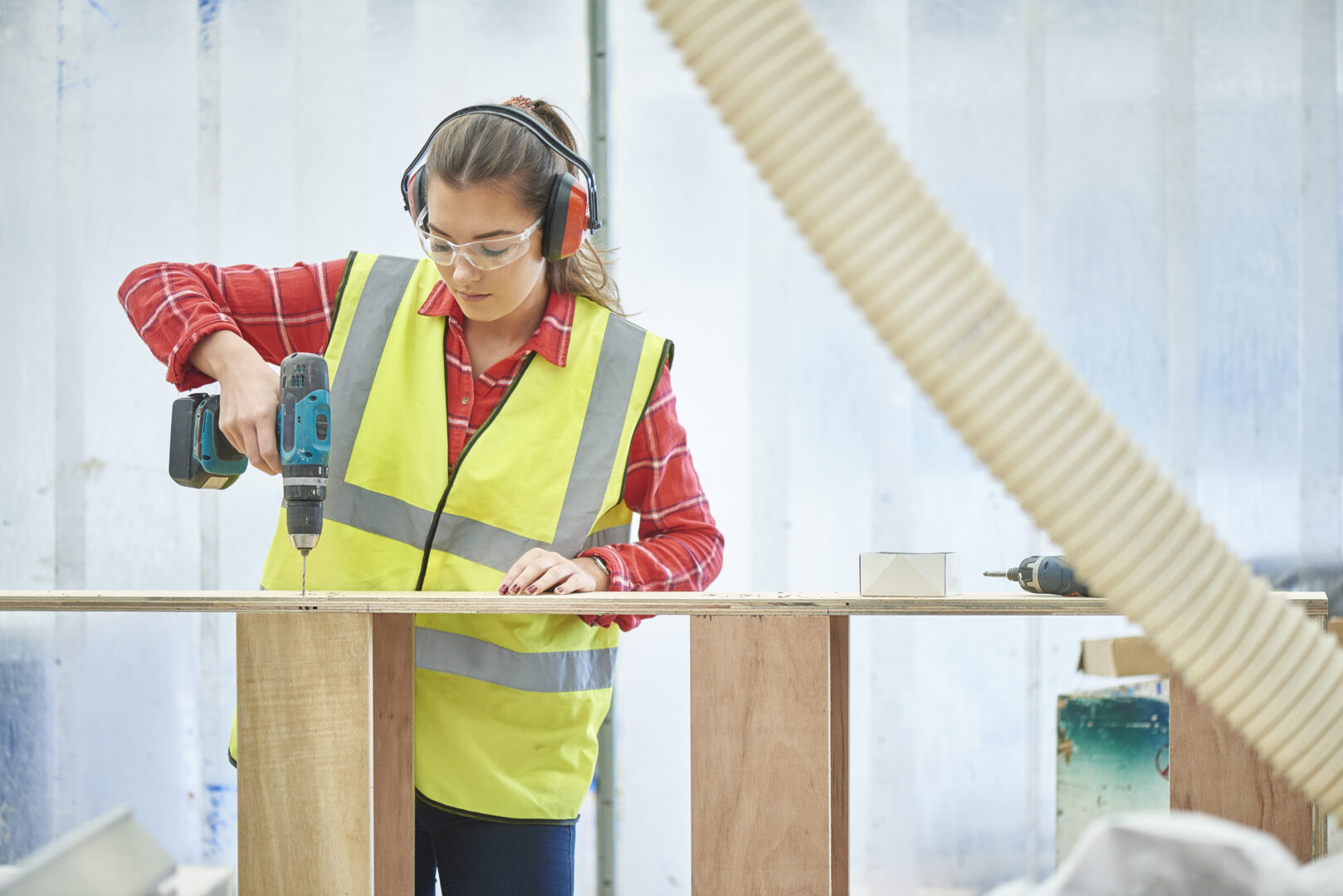 a female construction joinery student wearing protective gear as she drills a plank of wood