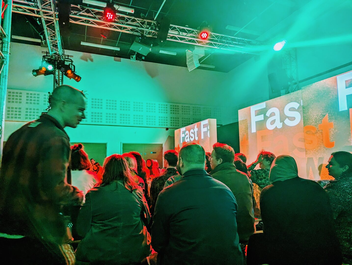 a crowd sat around a catwalk with lit up boards reading fast, fast, slow