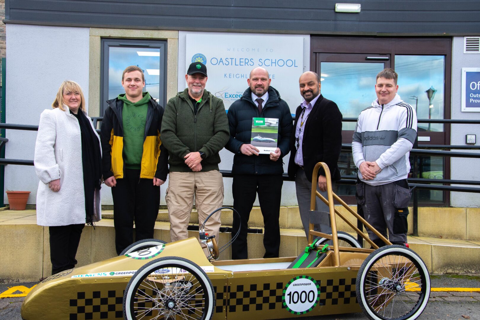 representatives from bradford college, greenpower and oastlers school in keighley pictured outside of oastlers school as they deliver a greenpower go kart to the school