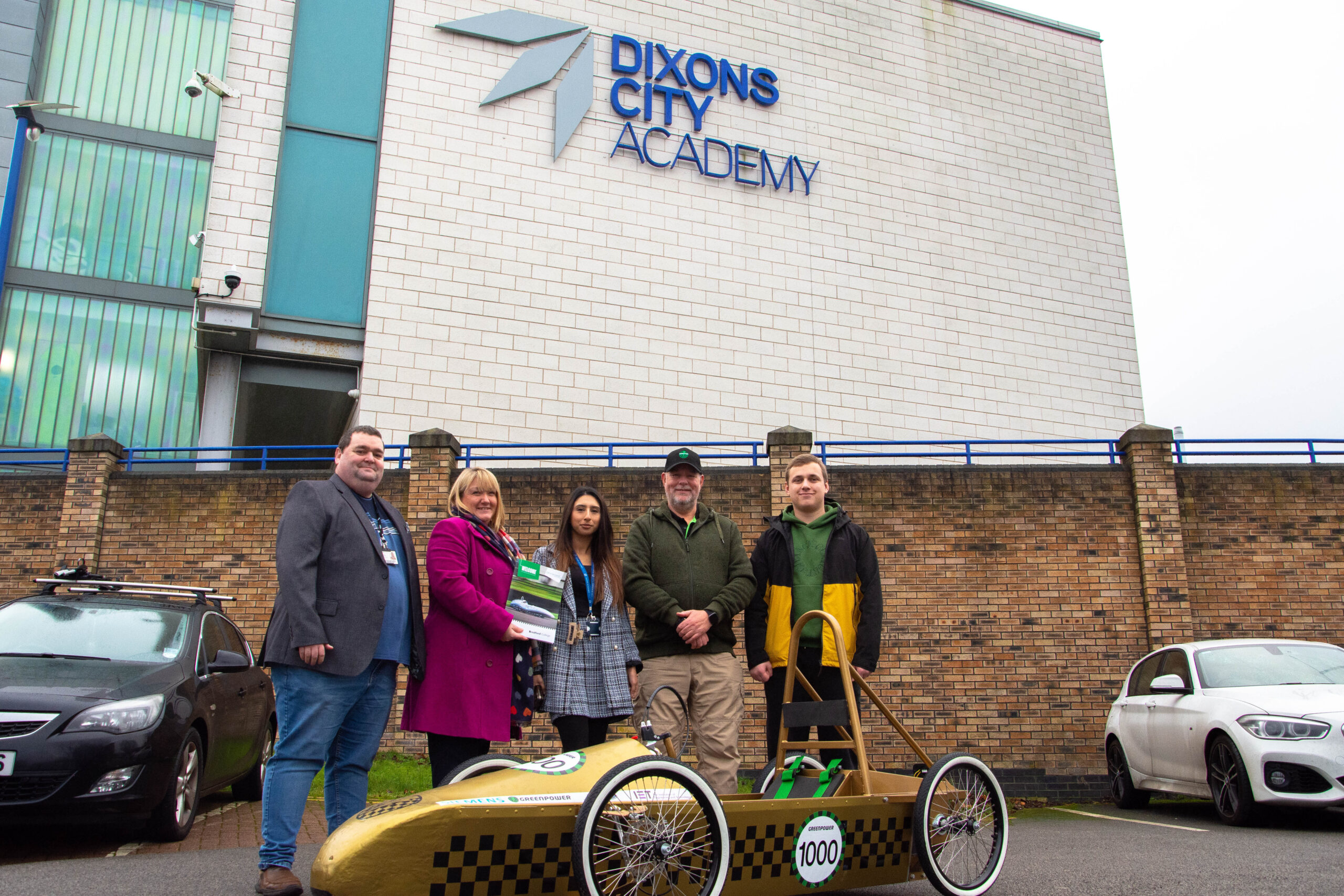 representatives from bradford college, greenpower and dixons city academy pictured outside of dixons city academy as they deliver a greenpower go kart to the school
