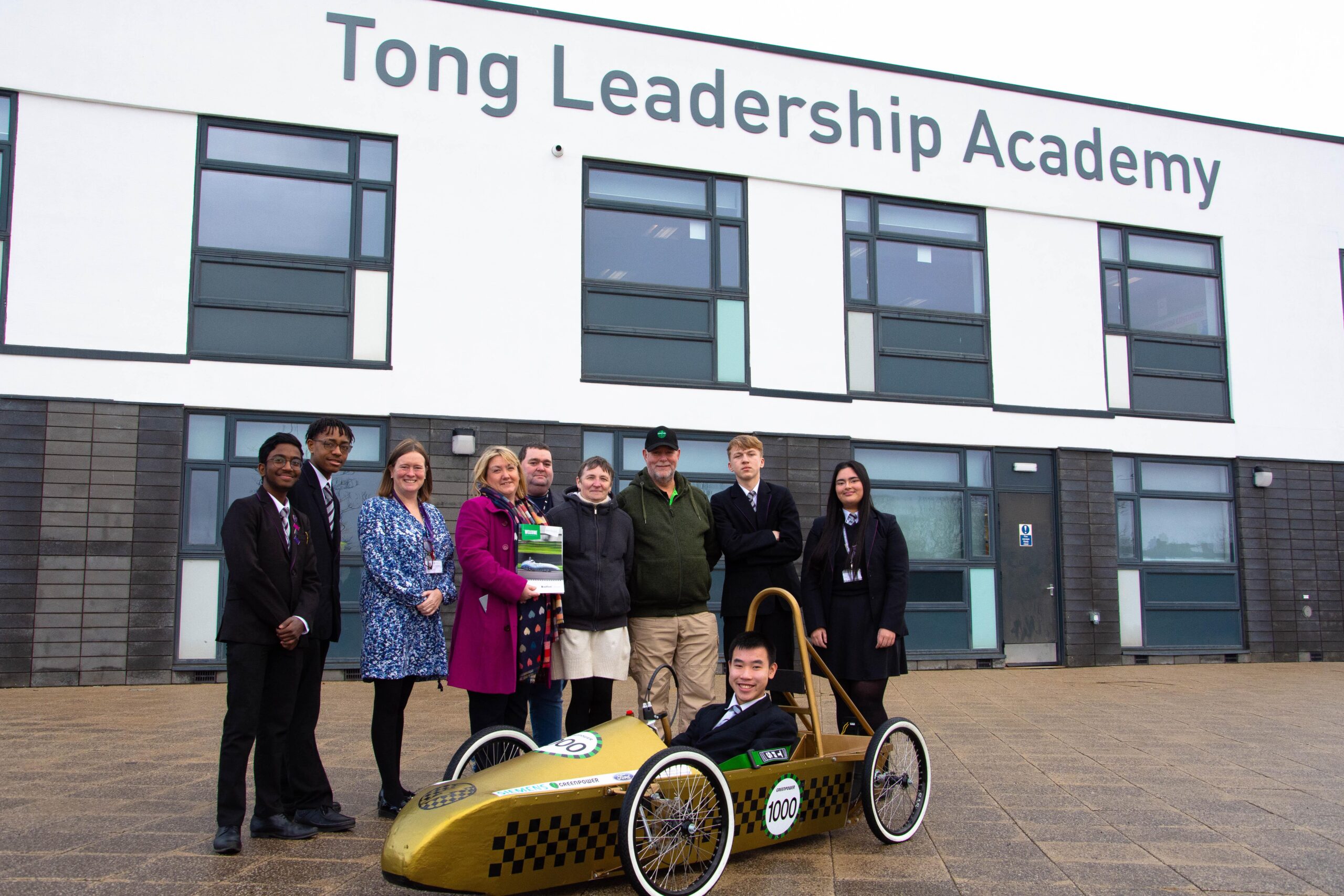 representatives from bradford college, greenpower and tong leadership academy pictured outside of tong academy as they deliver a greenpower go kart to the school