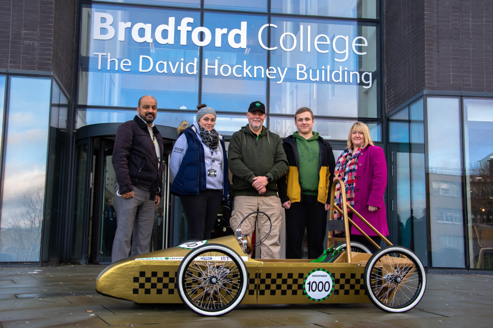 representatives from bradford college and greenpower pictured outside of the david hockney building as they deliver a greenpower go kart to the school