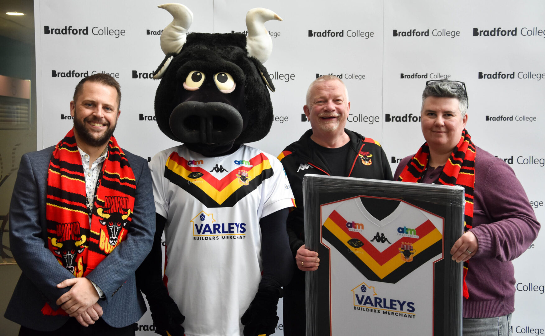 representatives from bradford college and bradford bulls stand with the bradford bulls mascot as they sign a new partnership deal