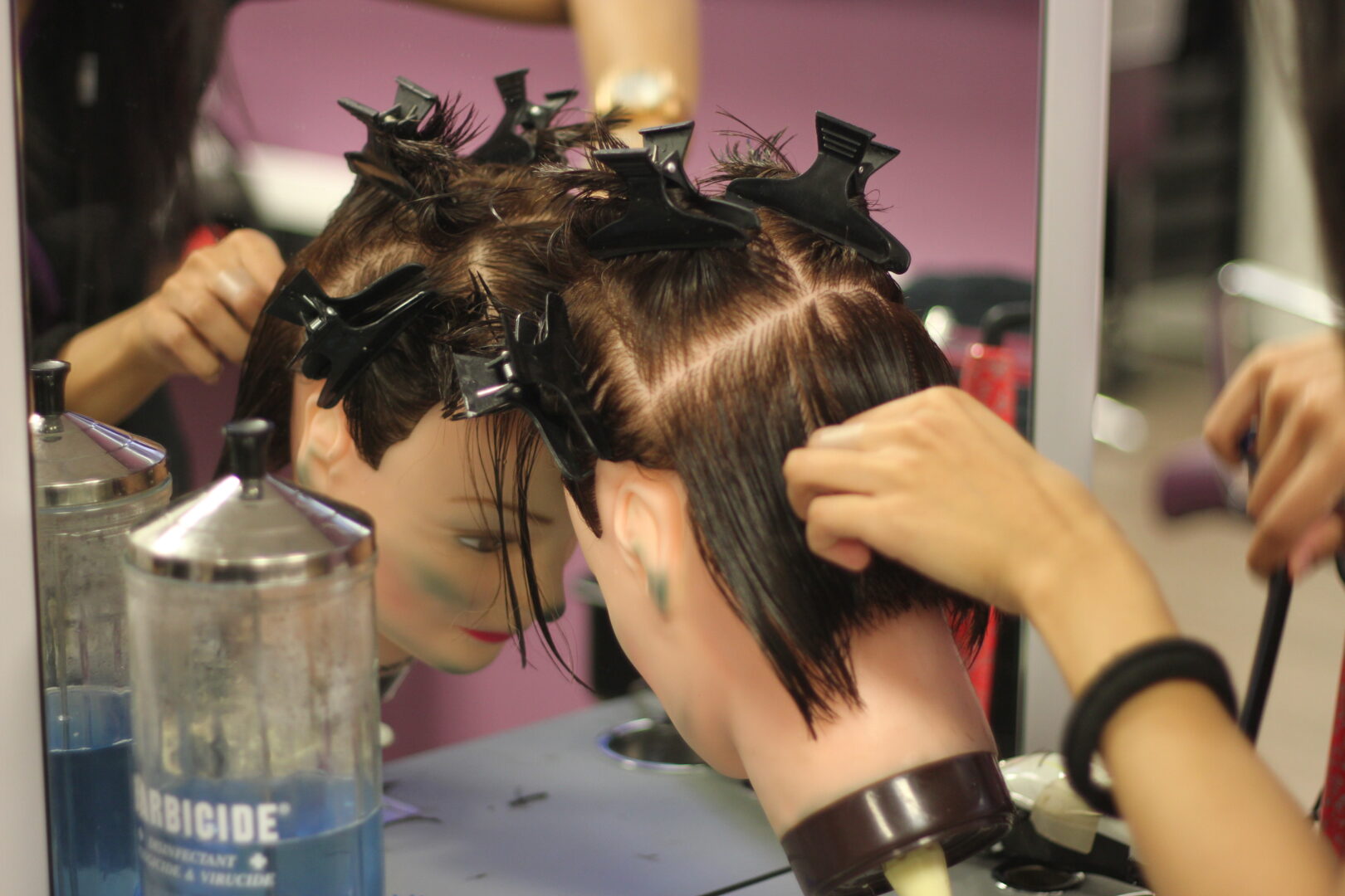 a student cuts the hair of a model head