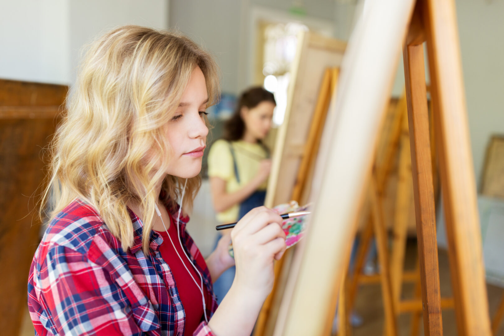 a young woman sits with a paintbrush in her hand painting on an easel