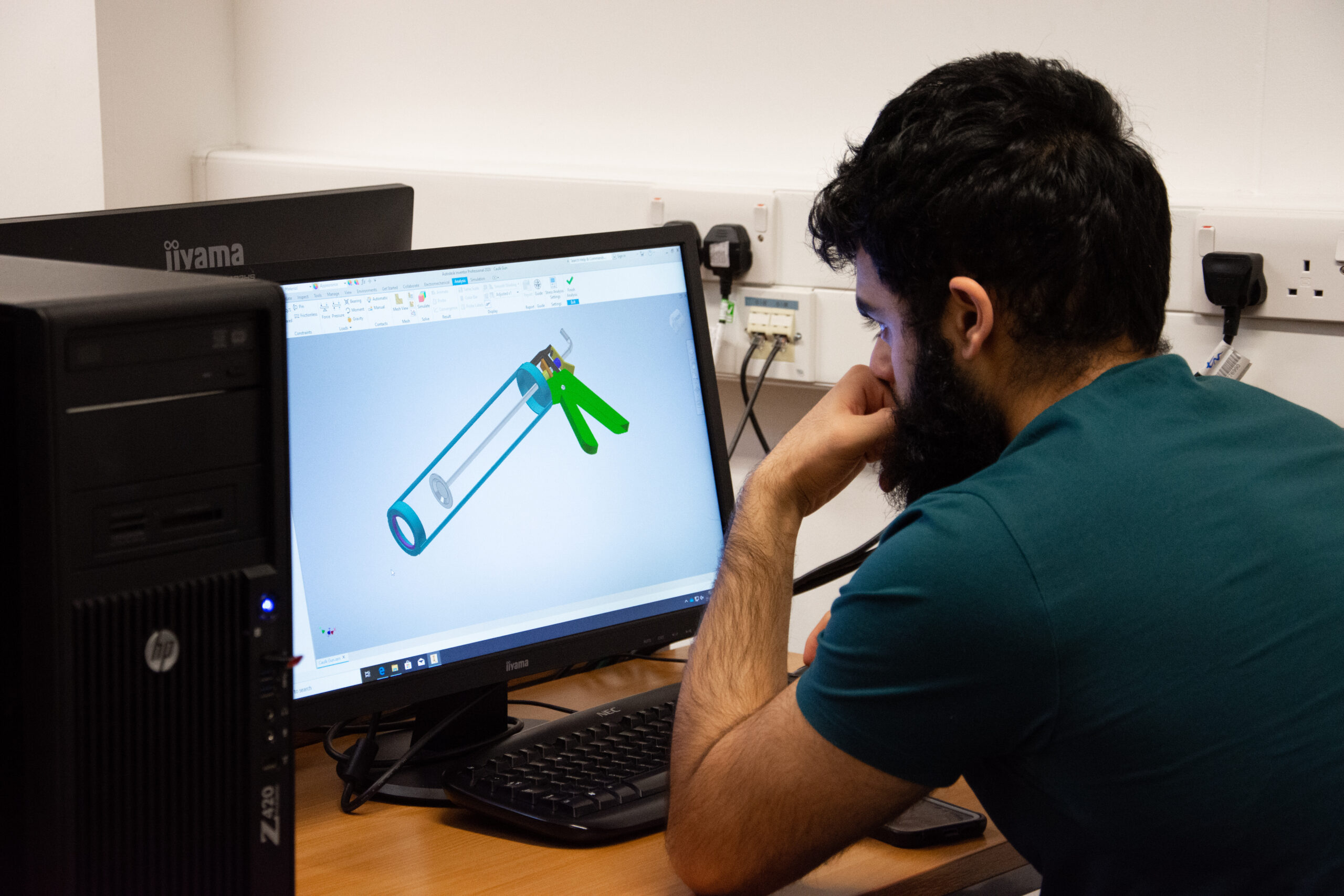 a student sits looking at a desktop computer working on mechanical engineering work