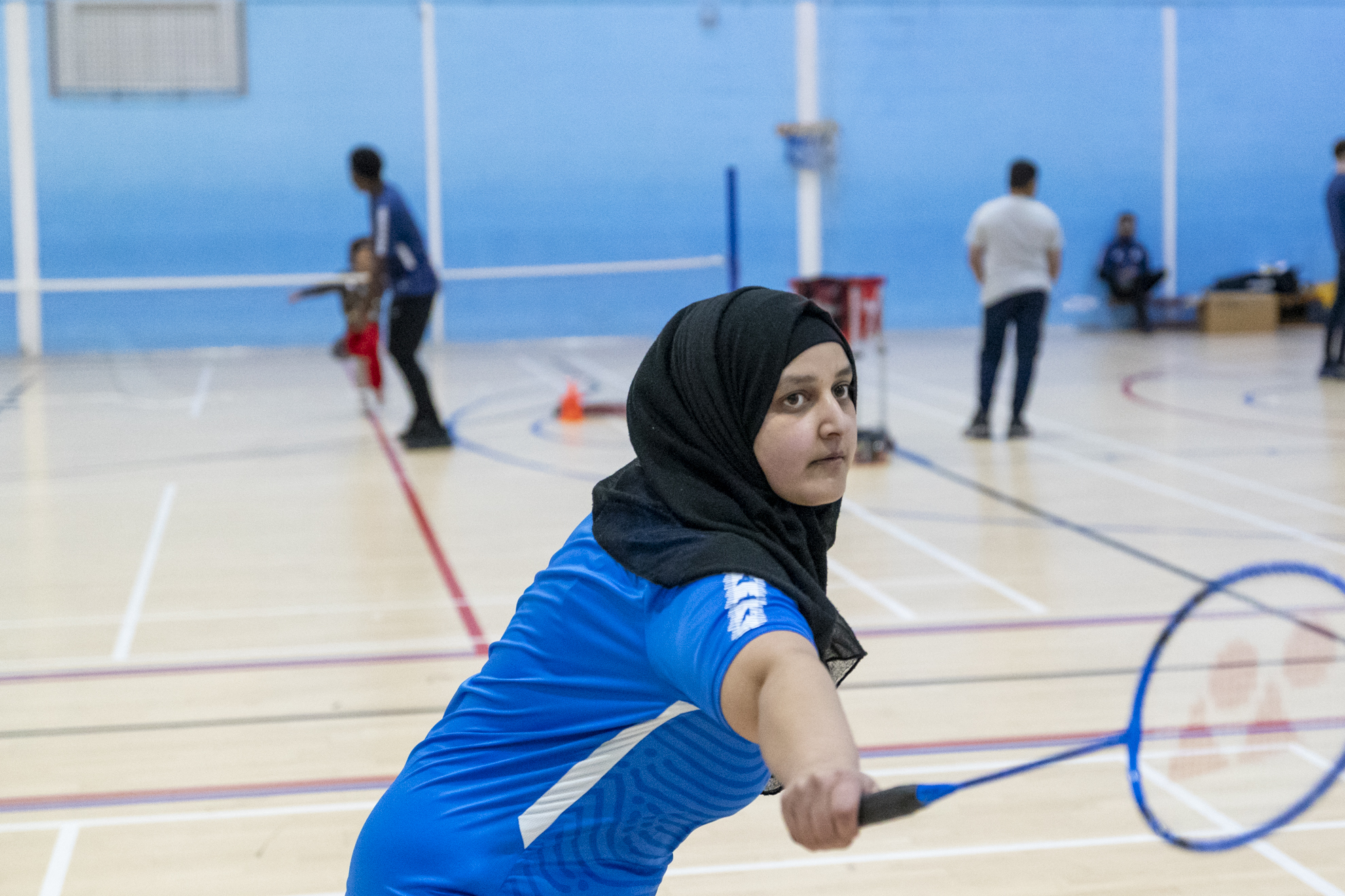 a female student stands in a sports hall holding a badminton racket stretching to hit the shuttlecock
