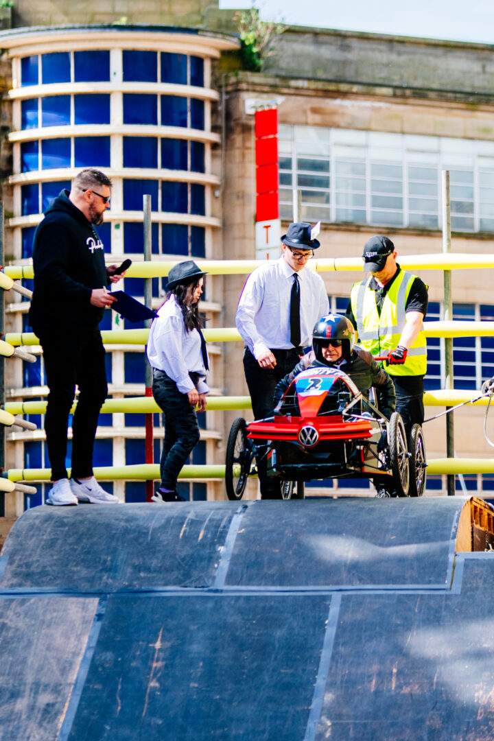 five team members stand on top of a slope, one sits in a go-kart