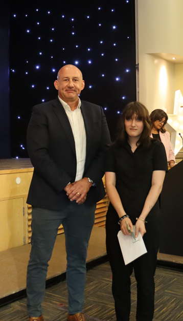 a student stands with an award and a certificate