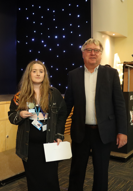 a student stands with an award and a certificate