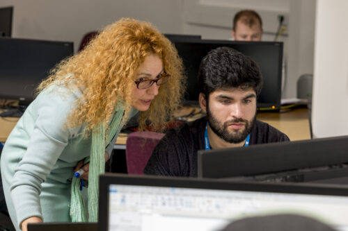 a student sits as a desk as a teacher looks over their work
