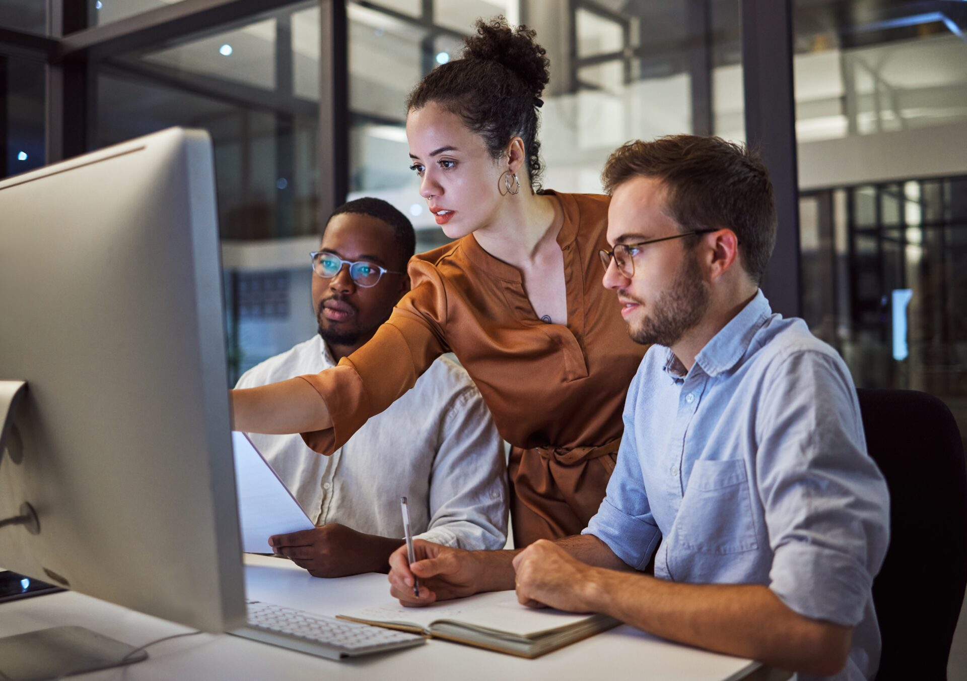 A woman pointing at a computer screen with 2 males