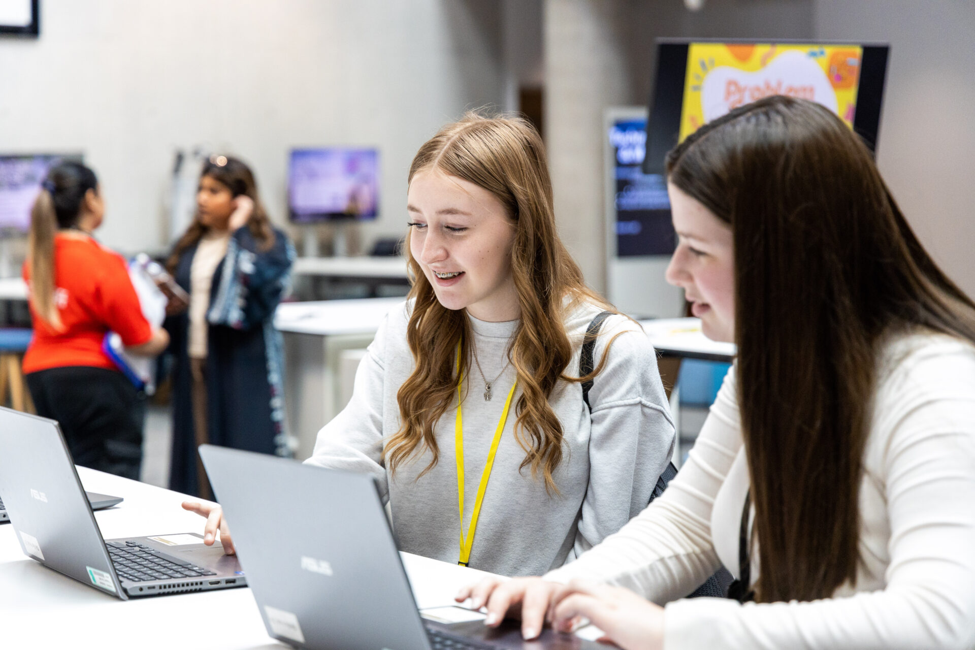 two students sit smiling working on laptops