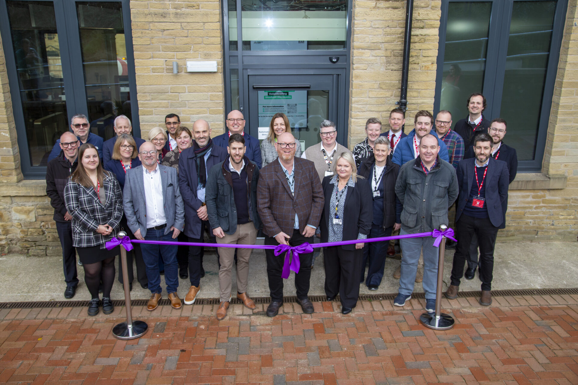 A group of people smiling as a purple ribbon is cut by Bradford College CEO, Chris Webb, to mark the opening of Garden Mills Building