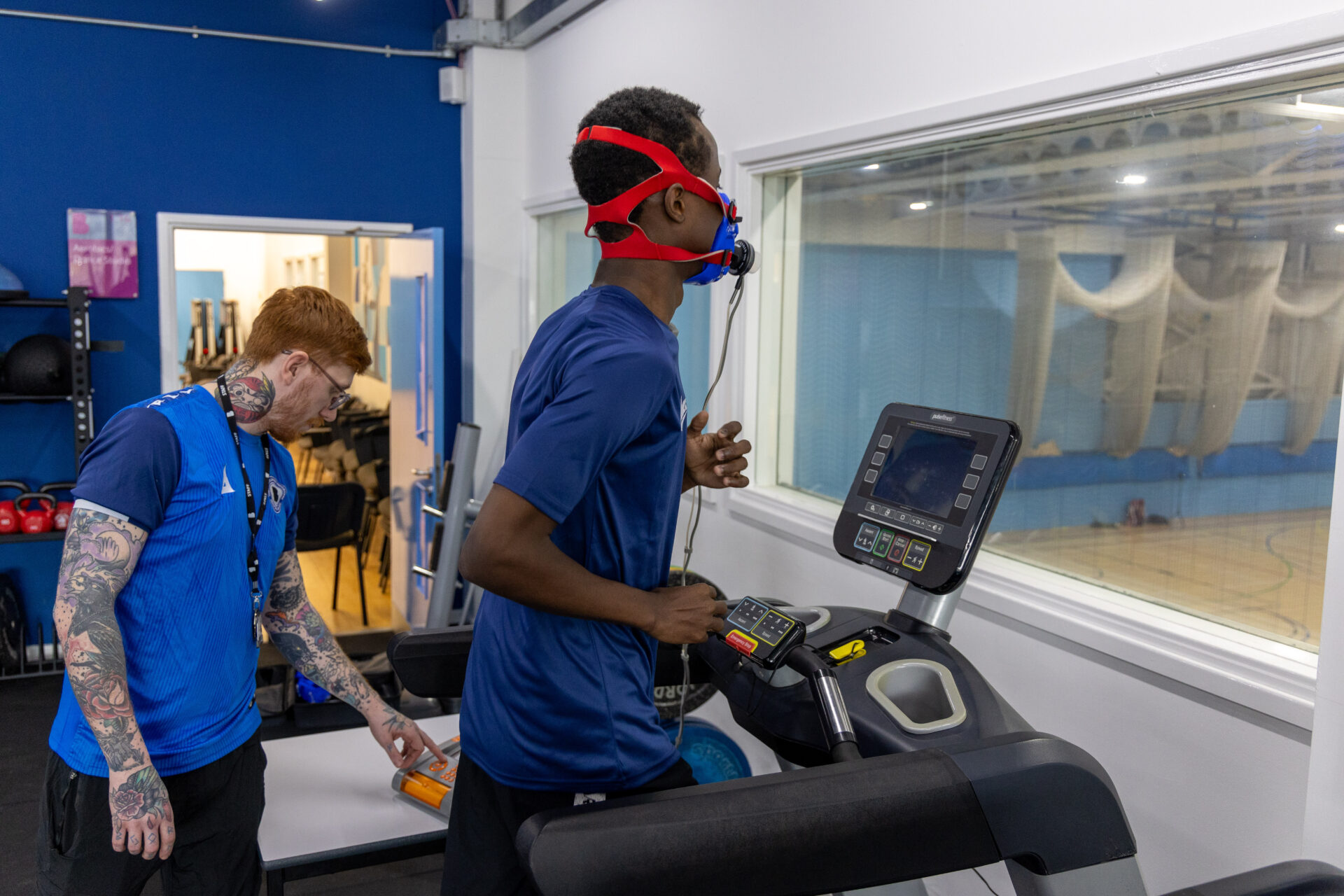 Man running on a treadmill wearing a breathing mask whilst another man looks at the information on the computer screen