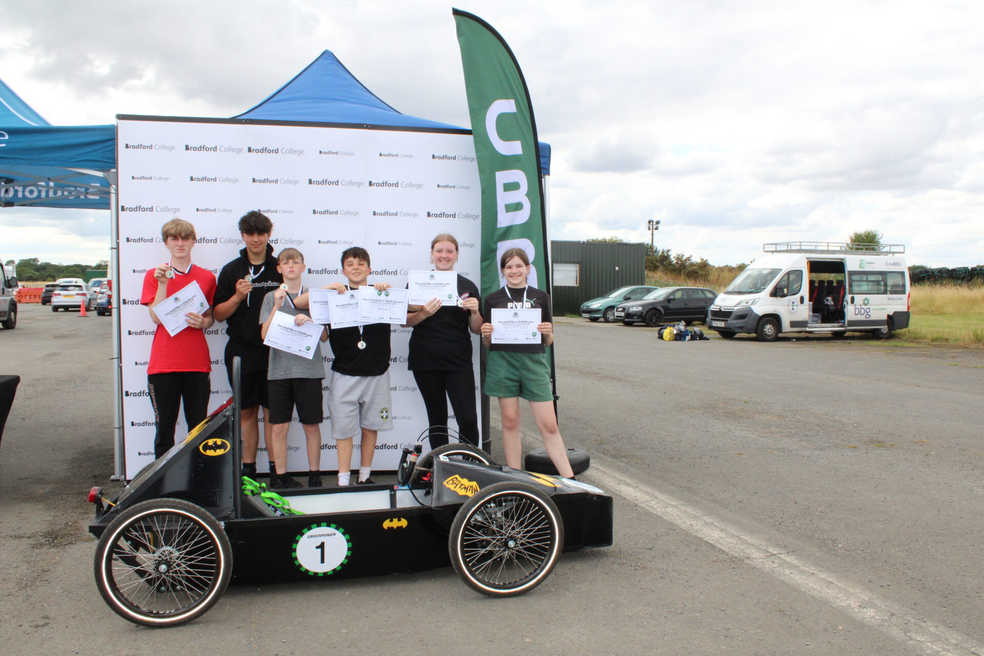 Group of students stood with certificates and a green power car in front of them