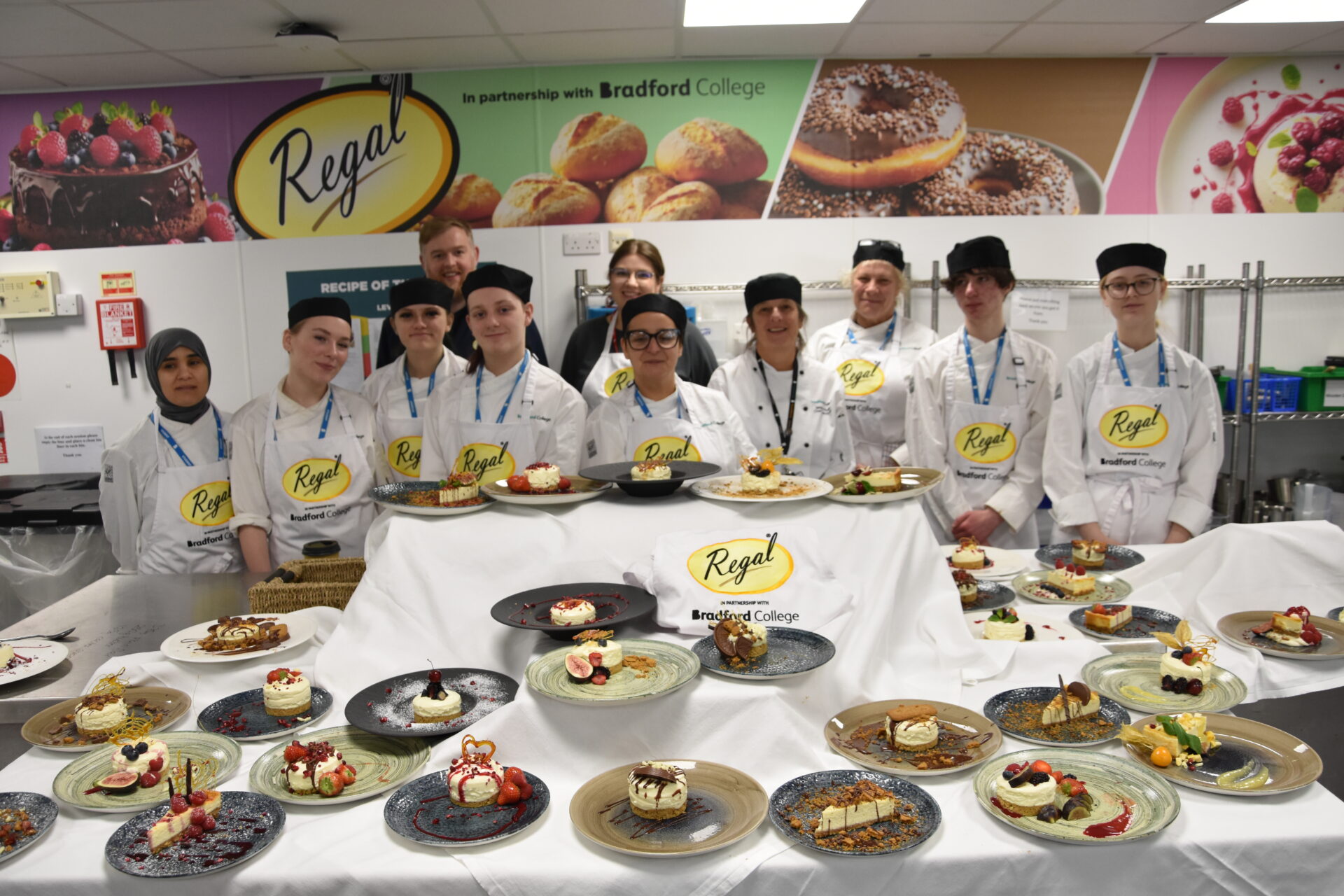 Group of students in aprons stood round a collection of cheesecakes