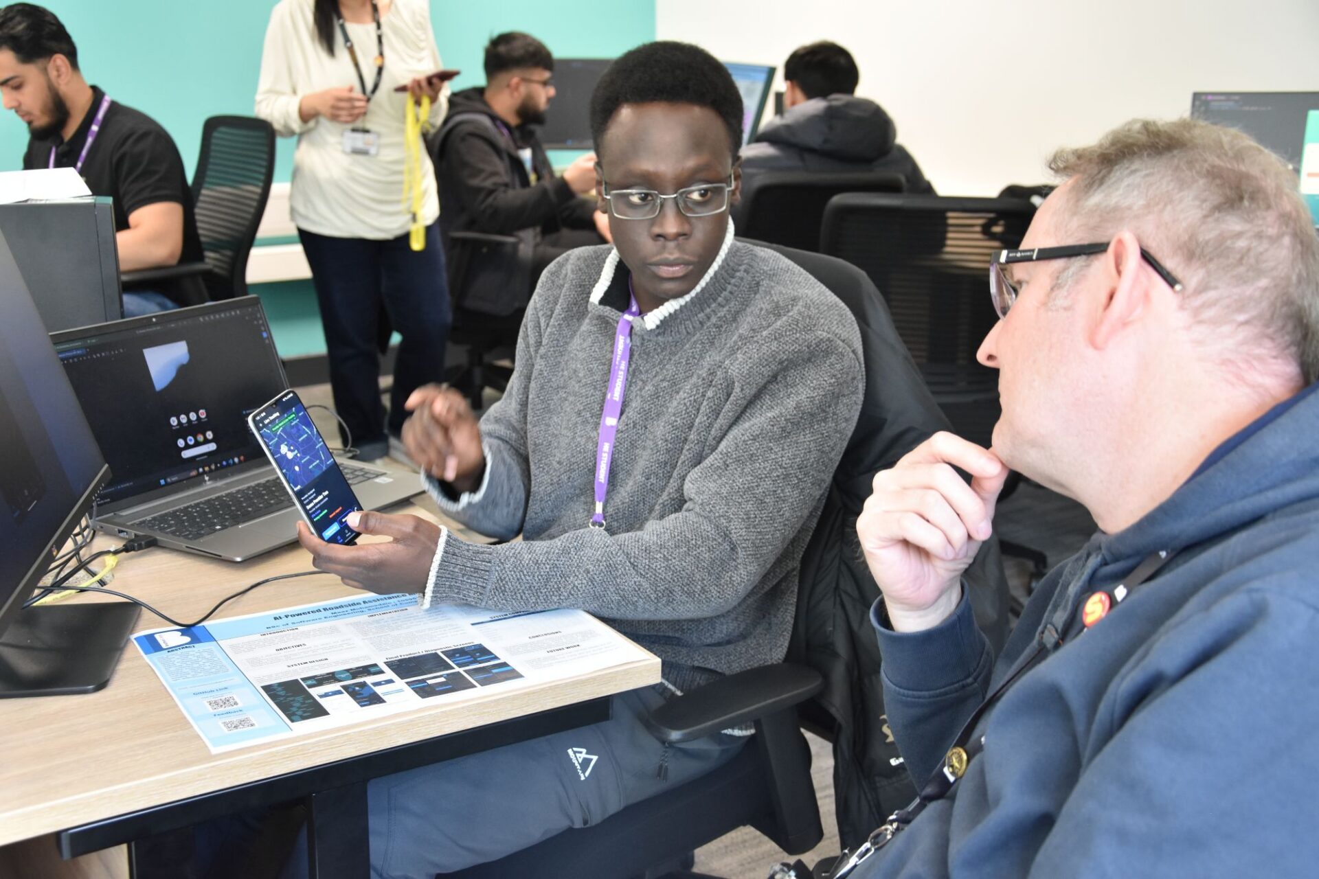Two men look at a phone screen and a presentation sheet talking.
