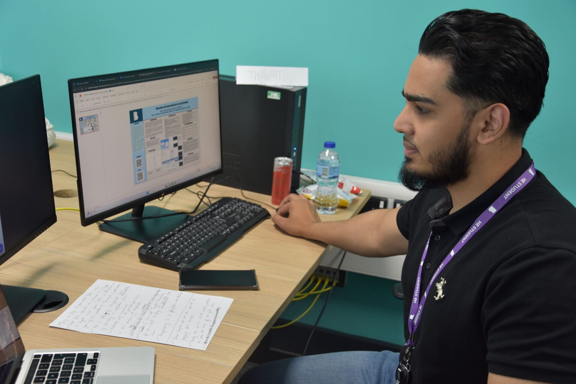 A male student sits at his desk in a classroom working on his end of year project displayed on the computer screen.