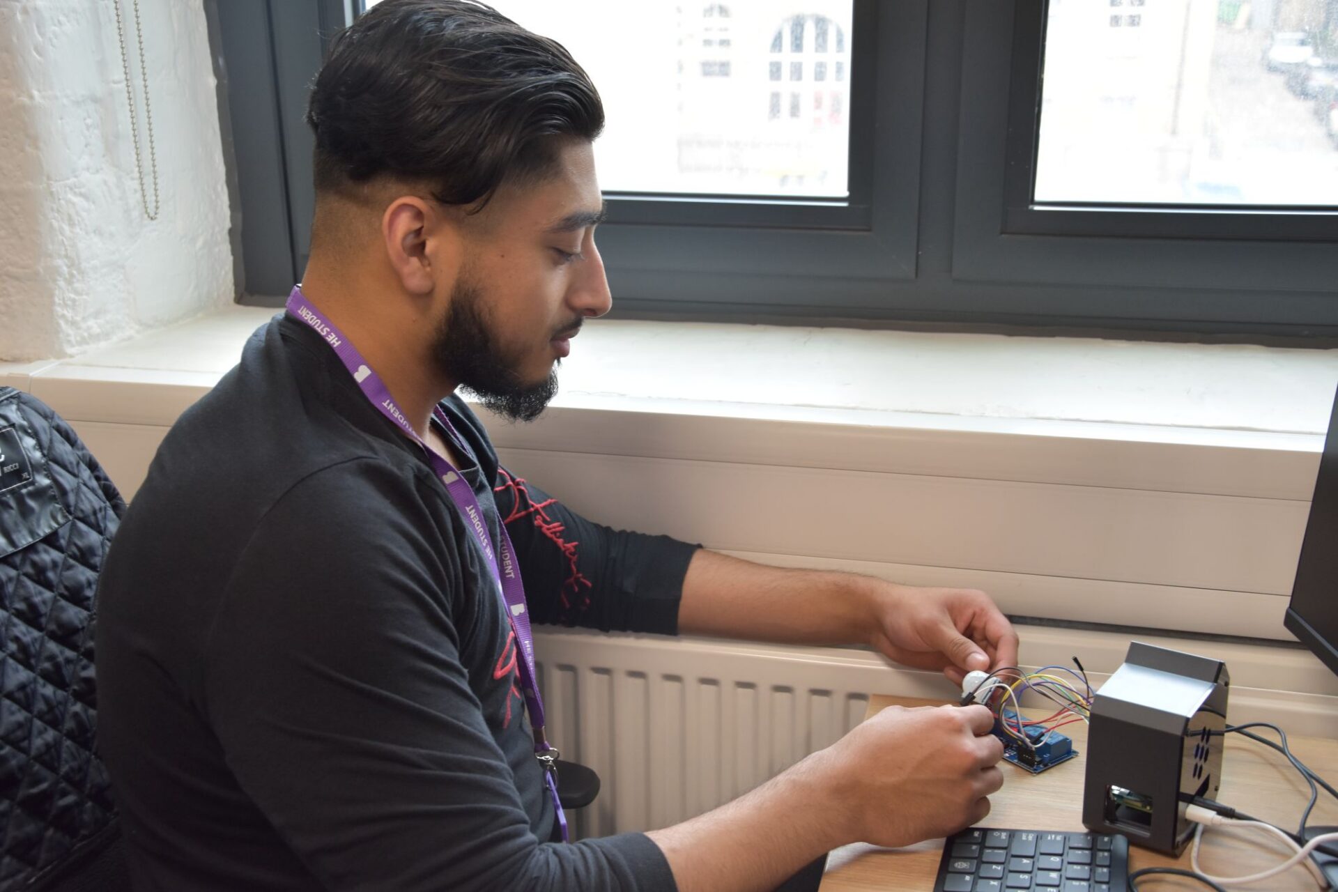 A male student works at his desk wiring a device as part of his end of year project.