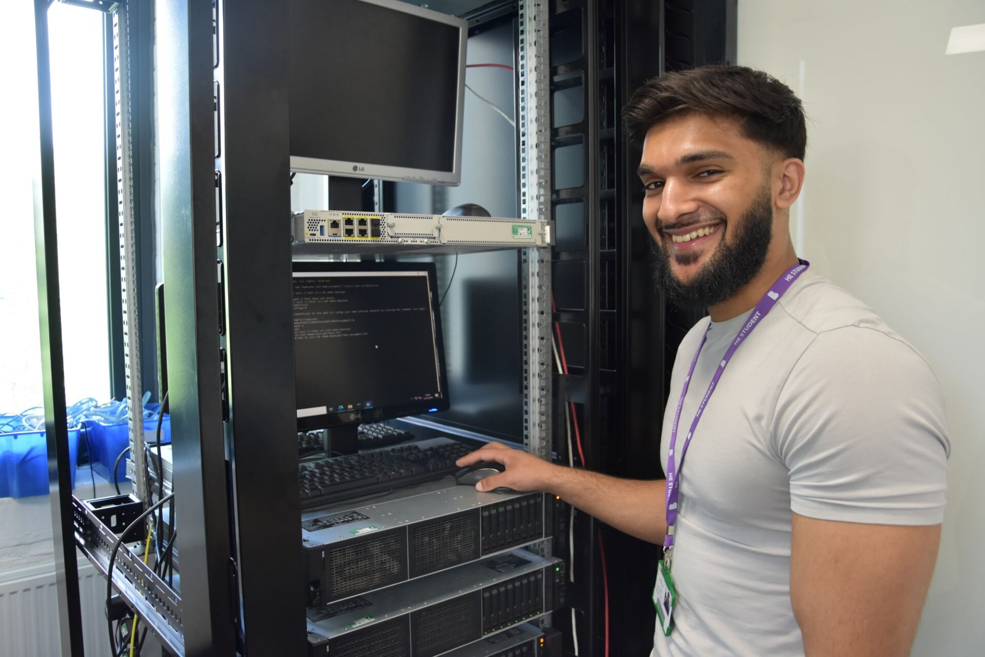 A male student stands smiling in front of a server unit he built.