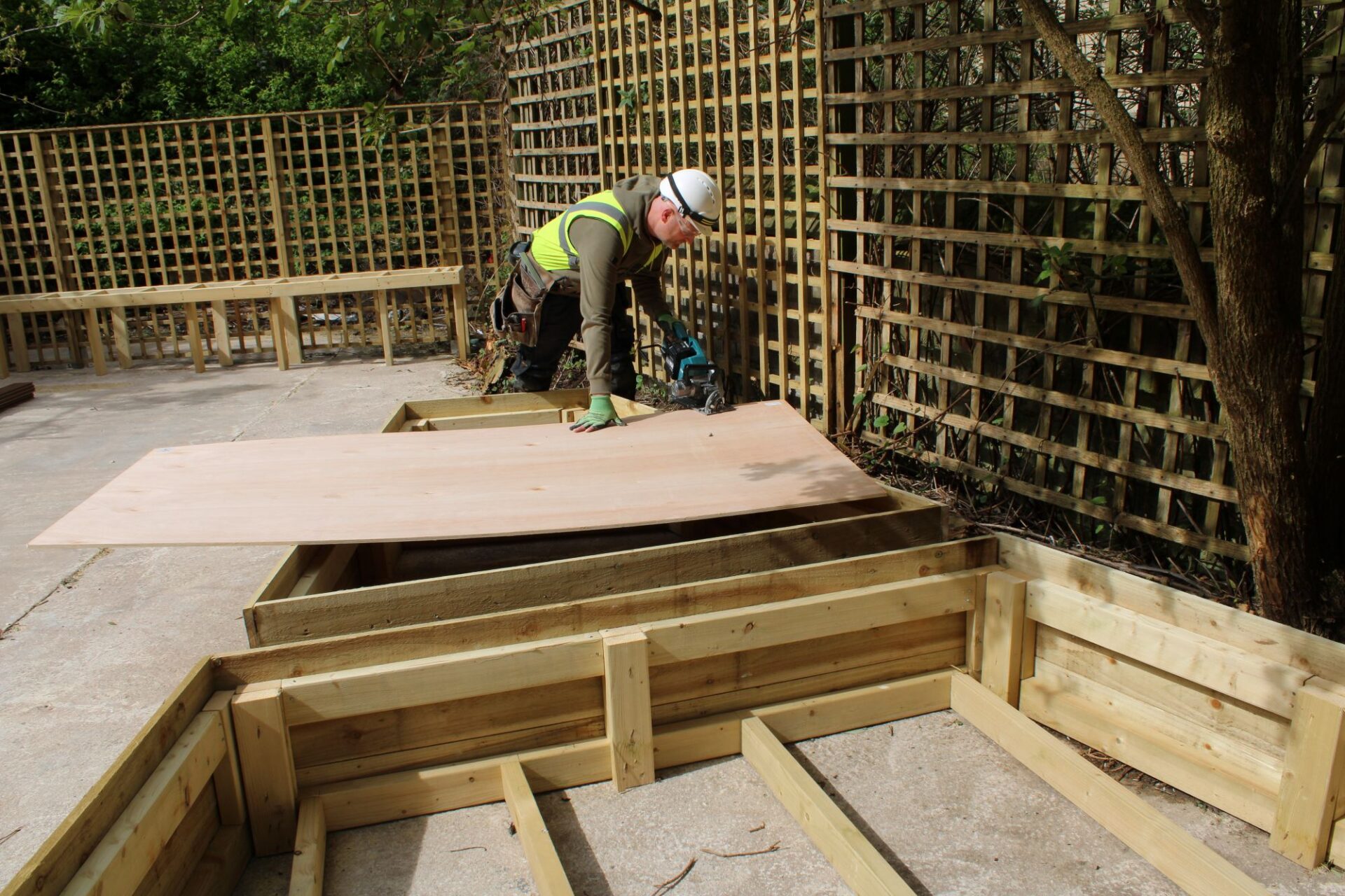 A man bends over while building a raised flower bed in the sunshine.